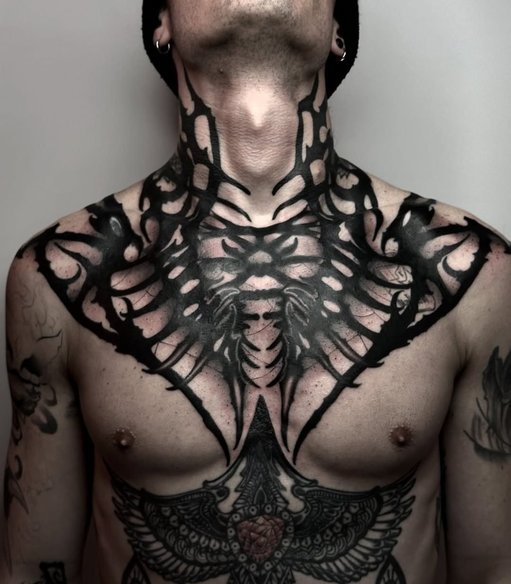 gothic blackwork tattoo covering chest and neck with dark symmetrical patterns and bold black ink design