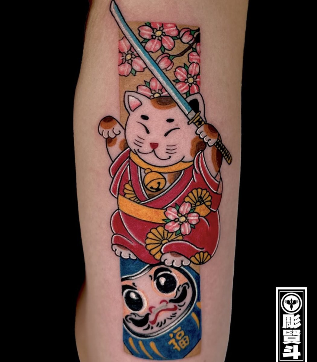 japanese style tattoo featuring a samurai cat holding a sword with traditional daruma doll and floral background
